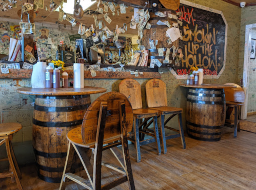 Rustic bar interior with wooden tables, chairs, and walls adorned with dollar bills and graffiti.