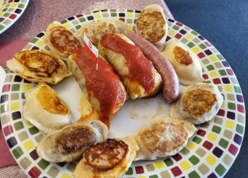 A colorful plate of pierogi, sausage, and stuffed cabbage topped with sauce, arranged on a patterned plate.