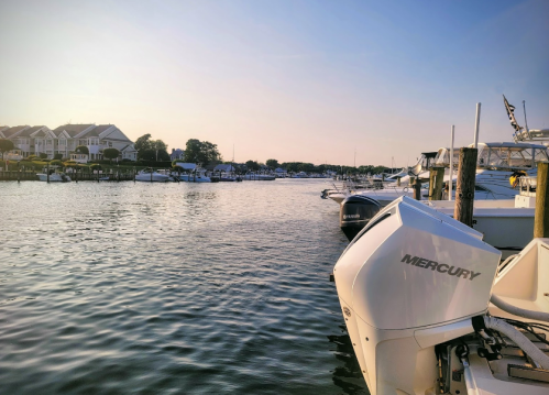 A peaceful marina at sunset, featuring boats and calm waters, with a Mercury outboard motor in the foreground.