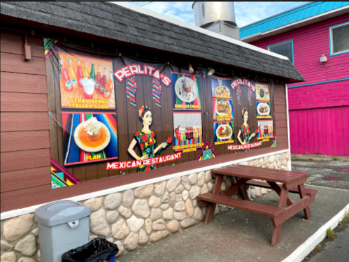 Colorful mural of a Mexican restaurant featuring food items and drinks, with a picnic table in front.