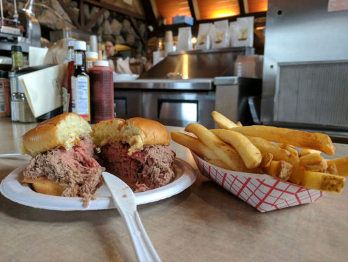 A plate with two halves of a beef sandwich and a side of fries, set in a casual dining environment.