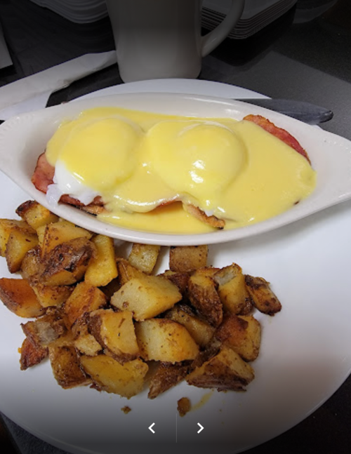 A plate of eggs Benedict with two poached eggs and hollandaise sauce, served with seasoned potato cubes.