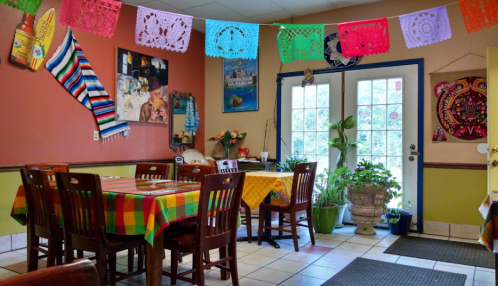Colorful restaurant interior with decorated walls, vibrant tablecloths, and plants, creating a warm, inviting atmosphere.