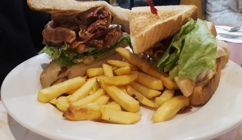 A plate with two large sandwiches filled with lettuce, bacon, and chicken, accompanied by a side of golden fries.