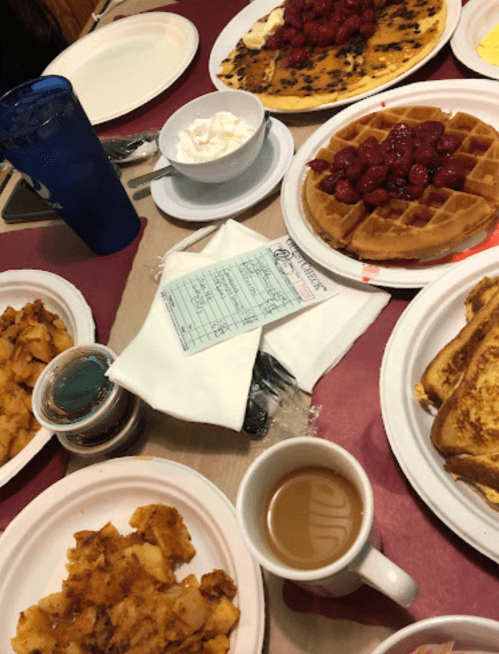 A table spread with various breakfast dishes, including waffles, French toast, potatoes, and a cup of coffee.