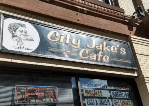 Sign for City Jake's Cafe featuring a cartoon chef and an "OPEN" neon sign, with menu items listed below.