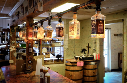 A rustic bar with hanging bottle lights, wooden decor, and a colorful countertop, creating a warm, inviting atmosphere.