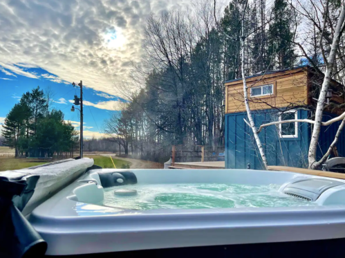 A hot tub with bubbling water, surrounded by trees and a blue sky with clouds in the background.