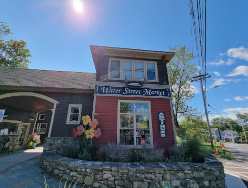 A charming market building with a sign reading "Water Street Market" and colorful flowers in front, set against a blue sky.