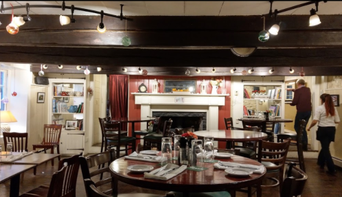 Cozy restaurant interior with wooden beams, tables set for dining, and warm lighting creating an inviting atmosphere.