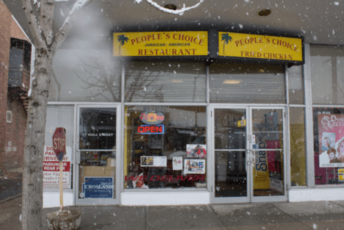 A snowy scene of the People's Choice Jamaican American Restaurant and Fried Chicken, featuring an open sign in the window.
