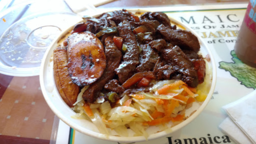 A bowl of Jamaican jerk chicken with plantains, vegetables, and a flavorful sauce on a colorful placemat.