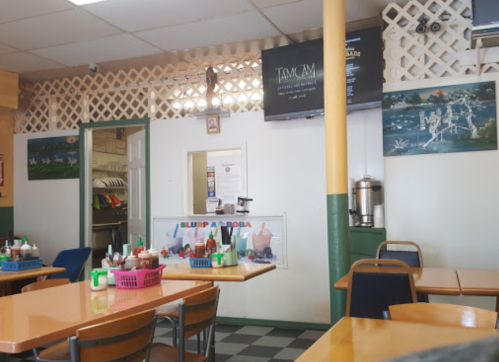 Interior of a casual restaurant with tables, condiments on the table, and a TV mounted on the wall.