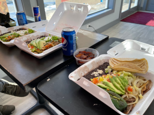 Two takeout containers with Mexican food, including rice, beans, salad, tortillas, and drinks on a table.
