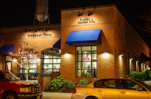 A brick building at night with blue awnings, featuring a restaurant and parked cars in front.