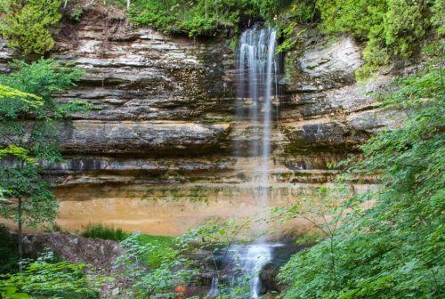 A serene waterfall cascading down rocky cliffs, surrounded by lush green foliage and trees.