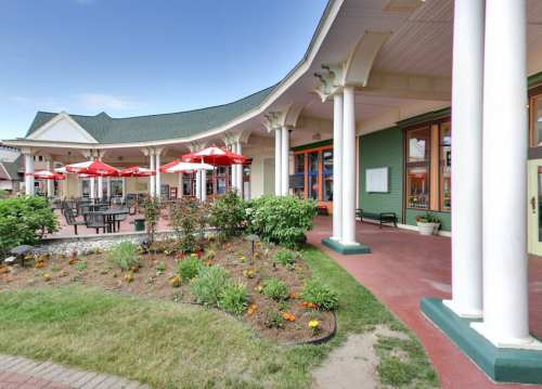 A charming building with a covered porch, colorful flowers, and outdoor seating under red umbrellas.