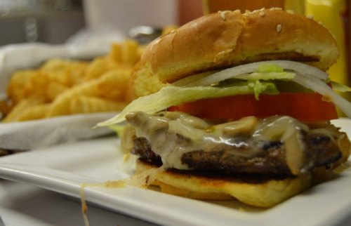 A close-up of a juicy burger with lettuce, tomato, and mushrooms, served with a side of crispy fries.