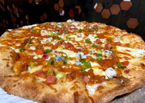 A close-up of a pizza topped with sauce, cheese, green onions, tomatoes, and blue cheese on a golden crust.