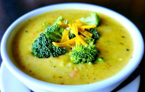 A bowl of creamy broccoli cheese soup topped with fresh broccoli and shredded cheddar cheese.