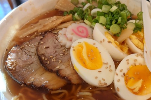 A bowl of ramen topped with sliced pork, soft-boiled eggs, green onions, narutomaki, and sesame seeds.