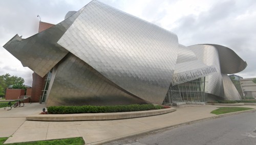 A modern, metallic building with a unique, sculptural design and large glass windows, surrounded by greenery.