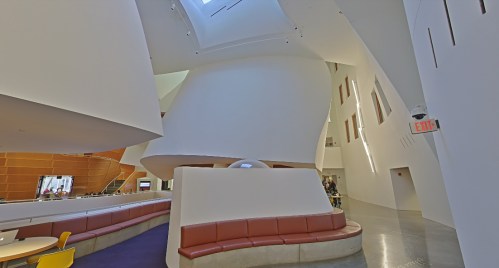Interior view of a modern, curved architectural space with white walls and a red seating area. Bright and open atmosphere.