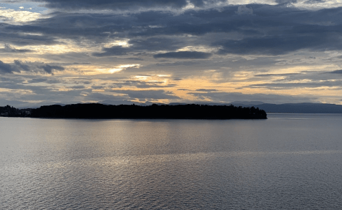 A tranquil lake scene at sunset, featuring calm waters and a distant island under a cloudy sky.