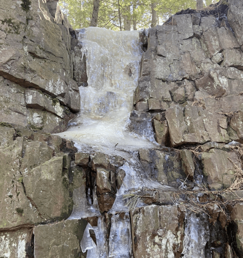 A small waterfall cascading over rocky terrain, surrounded by trees and natural vegetation.