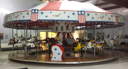 A vintage carousel with colorful horses, decorated with red, white, and blue stars, inside a museum.