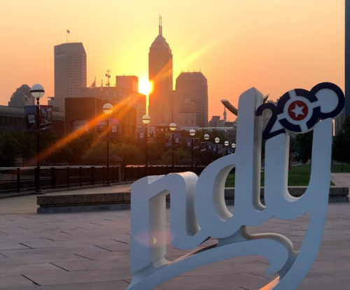 Sunset over a city skyline with a large "ndy" sign in the foreground, casting a warm glow on the scene.