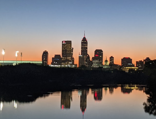 City skyline at dusk, reflecting on water, with lights twinkling against a gradient sky.