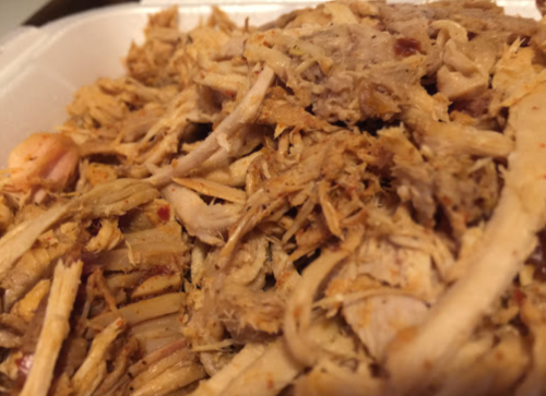 Close-up of shredded, seasoned pulled chicken in a white takeout container.