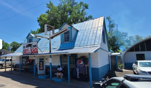 A blue and white building with a metal roof, featuring a BBQ sign and outdoor seating area.