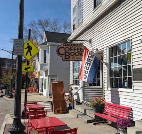 A coffee shop with a sign reading "Crackskull's Coffee & Books," featuring outdoor seating and a nearby pedestrian crossing sign.