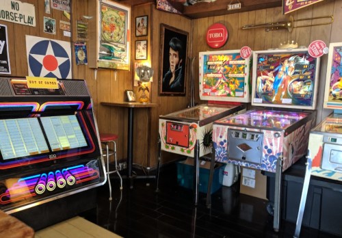 A retro arcade room featuring pinball machines, a jukebox, and vintage decor on wooden walls.