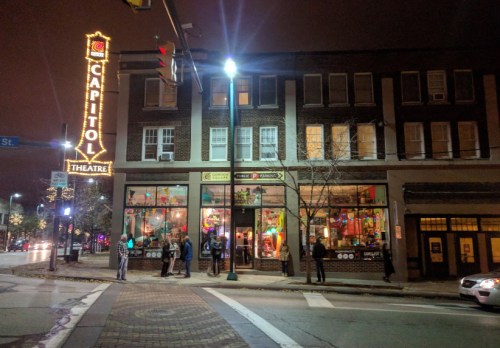 A brightly lit theater building at night, featuring a marquee sign and people gathered outside.