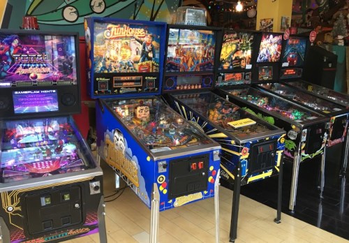 A row of colorful pinball machines in a vibrant arcade setting.