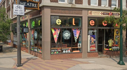 Colorful storefront with "super elect" signage, large windows, and decorative banners in a vibrant urban setting.