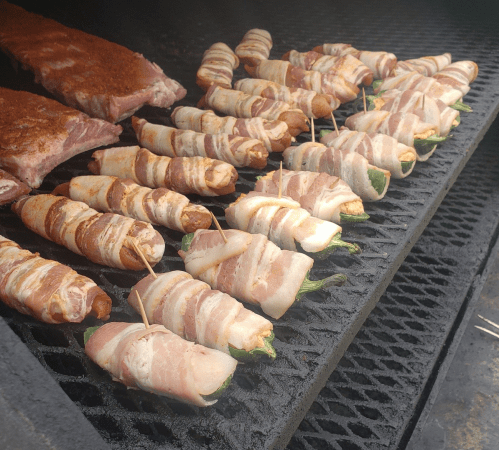 Bacon-wrapped jalapeño poppers and sausages grilling on a barbecue.