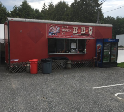 A red food truck with a BBQ sign, featuring a window for orders and a Pepsi vending machine nearby.