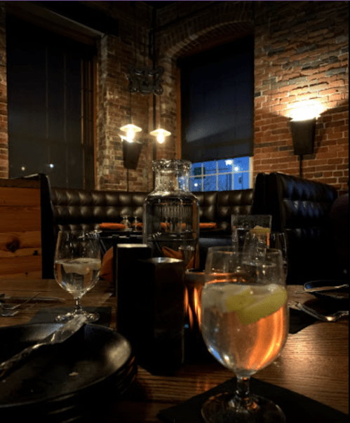 A cozy restaurant interior with brick walls, dim lighting, and tables set with drinks and plates.
