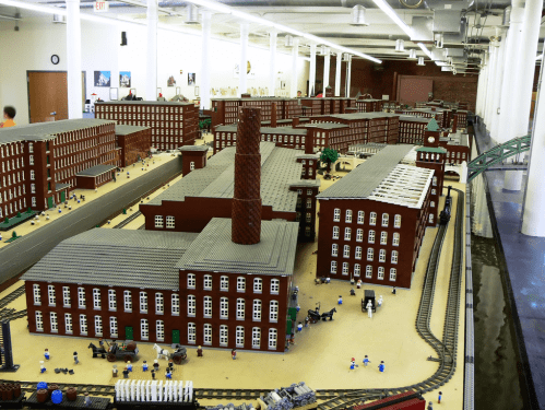 A detailed model of a factory complex made from bricks, featuring buildings, tracks, and miniature figures.