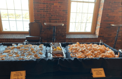 A seafood display featuring oysters on one side and a shrimp cocktail on the other, set against brick walls and windows.