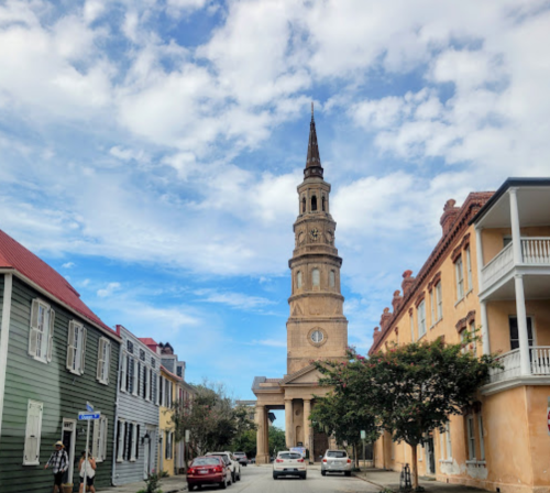 Historic street view featuring a tall church steeple, colorful buildings, and a blue sky with scattered clouds.