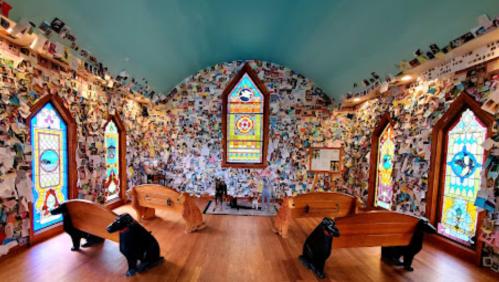A room with colorful stained glass windows, walls covered in photos, and two wooden dog sculptures near wooden coffins.