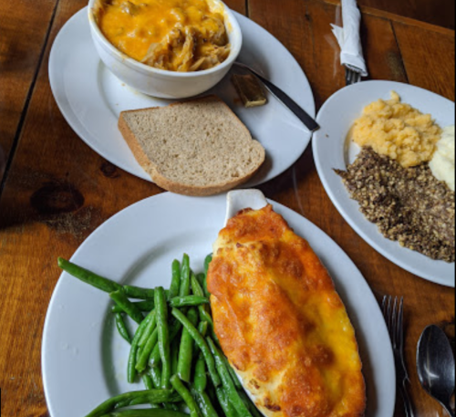 A plate with green beans, a cheesy casserole, and a side of bread, alongside another plate with mashed potatoes and stuffing.