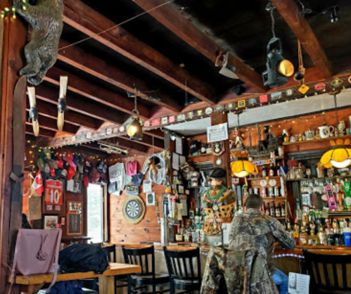 Cozy bar interior with wooden beams, vintage decor, and a patron sitting at the counter.