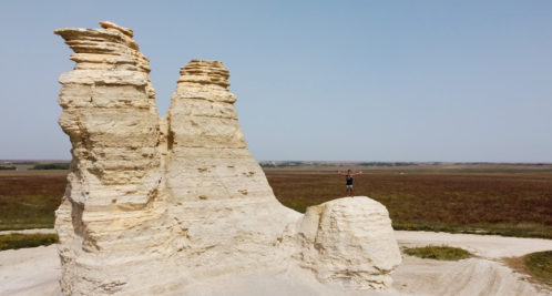 A person stands on a rock formation in a vast, open landscape under a clear blue sky.