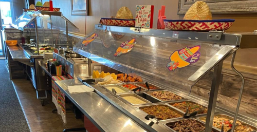 A vibrant buffet with various dishes, decorated with sombreros and colorful signs, in a restaurant setting.